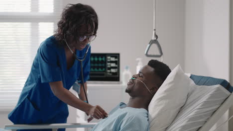 A-black-female-doctor-is-talking-to-a-black-male-patient-lying-on-a-hospital-bed-and-connected-to-an-acid-supply